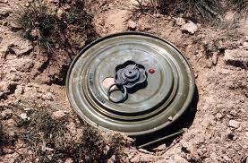 A round metal landmine partly buried in dry soil